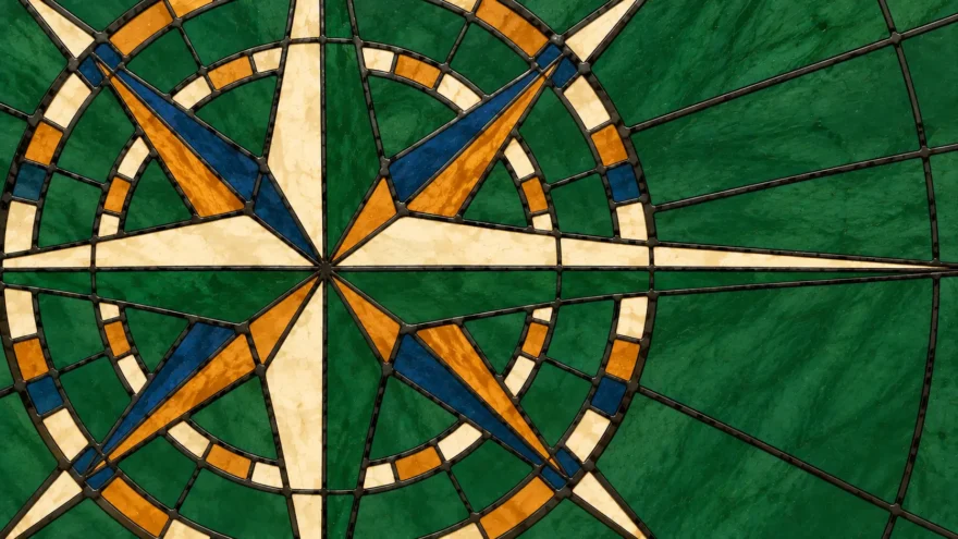 A stained glass panel of an eight-point compass rose in cream, ochre and blue, ringed by two banded circles on a deep green field.
